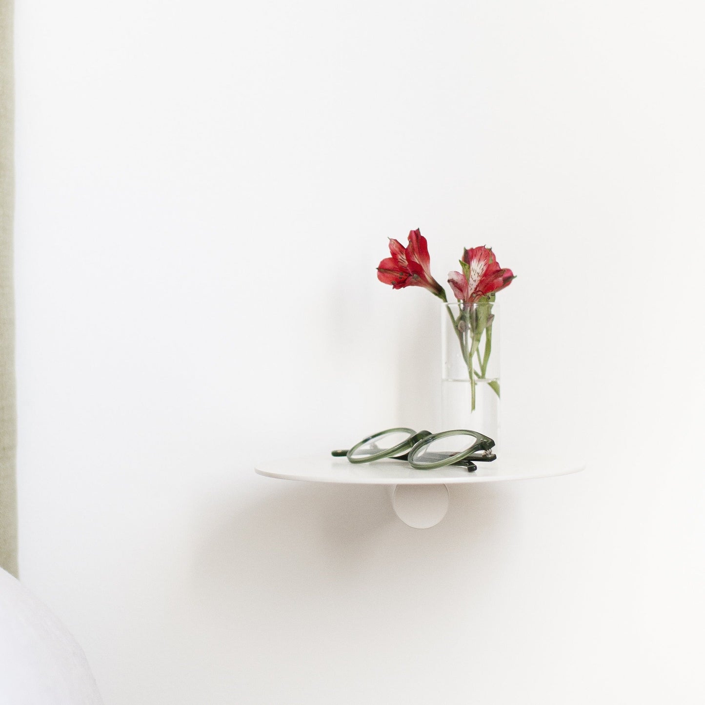 Vägghylla Platå i creme – rund, svävande vägghylla i pulverlackat stål, använd som sängbord med blommor